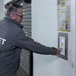 Imaginea prezintă o persoană la panoul de control al unui sistem automatizat de parcare, care confirmă procesul de stocare și astfel inițiază transportul automat al vehiculului către un loc de parcare disponibil.
