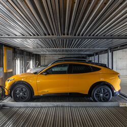 Imaginea prezintă o mașină pe o platformă într-un sistem de parcare automatizat din interiorul unei parcări subterane moderne.