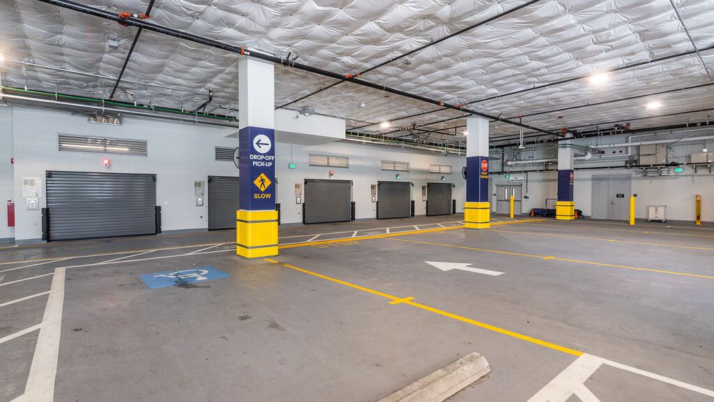 Imaginea prezintă intrarea într-un sistem de parcare automatizat dintr-o parcare subterană modernă, cu mai multe porți de acces.