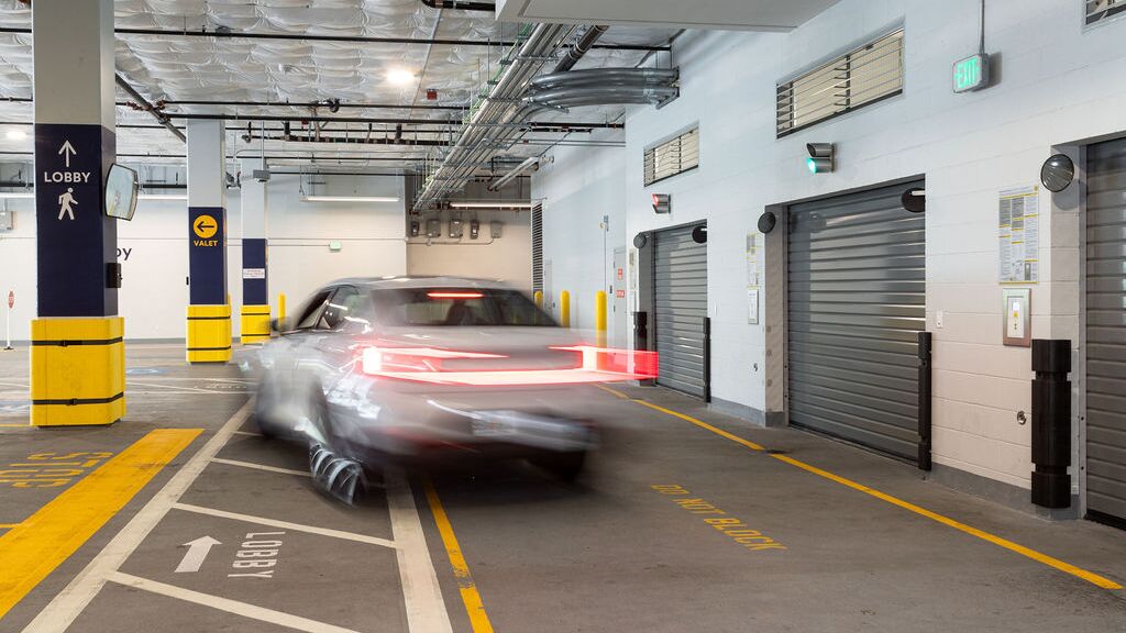 Imaginea prezintă un vehicul care intră într-un sistem de parcare automatizat dintr-o parcare subterană modernă, cu mai multe porți de acces.