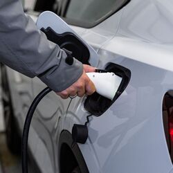 Imaginea prezintă procesul de încărcare a unui vehicul electric, în cadrul căruia un conector de încărcare este conectat la vehicul pentru a încărca bateria în timpul procesului de parcare.
