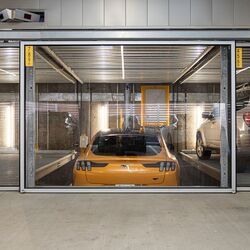 Imaginea prezintă o mașină sport galbenă într-un sistem de parcare din interiorul unei parcări subterane moderne.