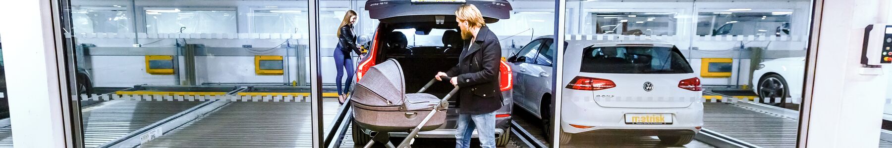 A car park with parked cars and a person pushing a pram