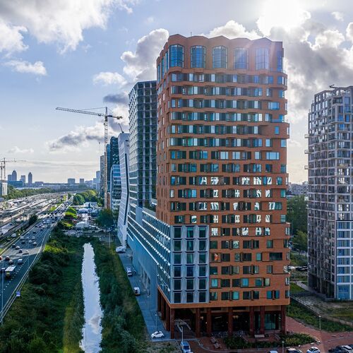 Vedere exterioară a proiectului The Pulse din Amsterdam, cu clădiri înalte moderne și infrastructură urbană de transport.